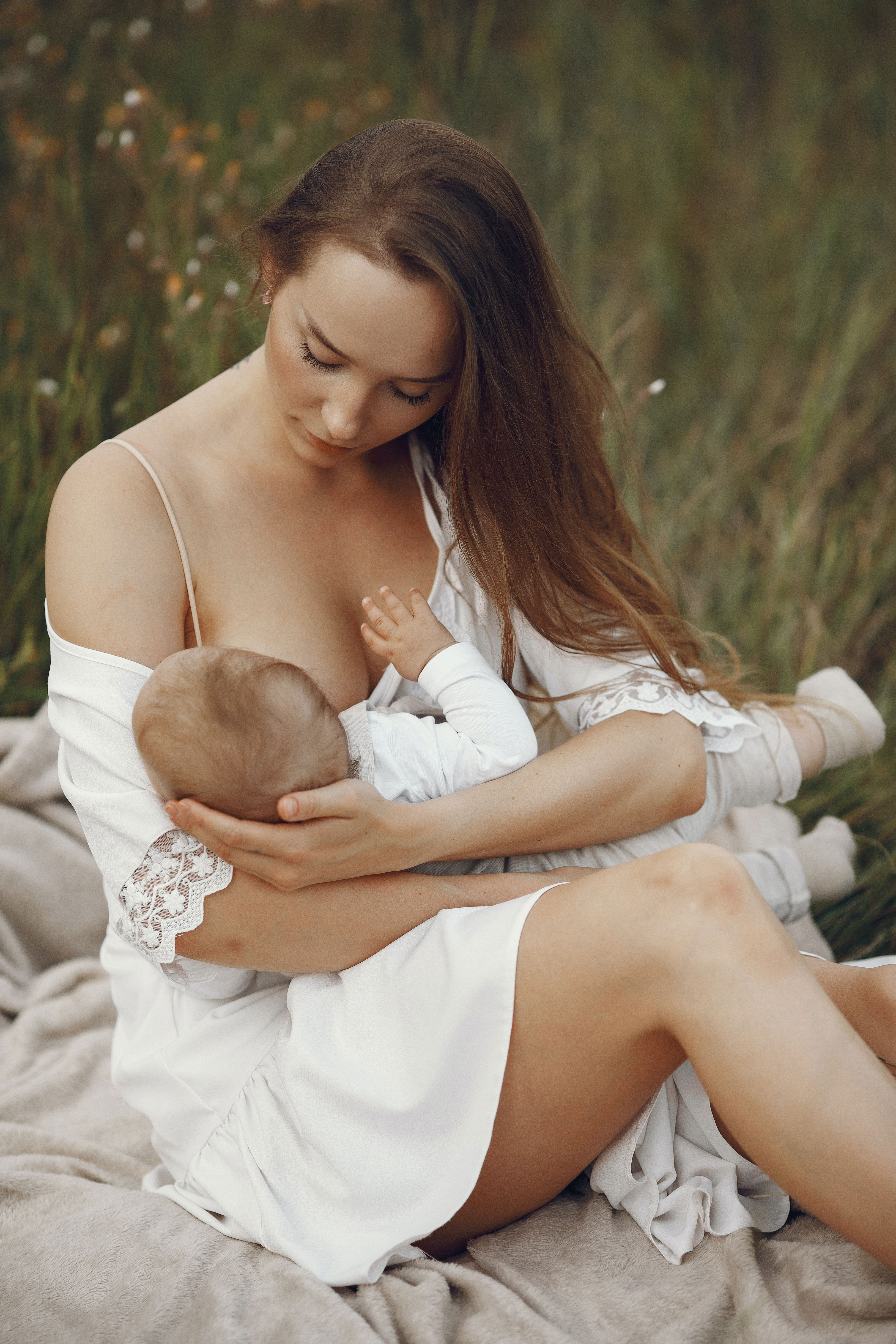 A woman holding her baby in the grass.