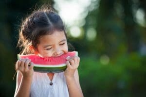 A little girl holding up a piece of watermelon.